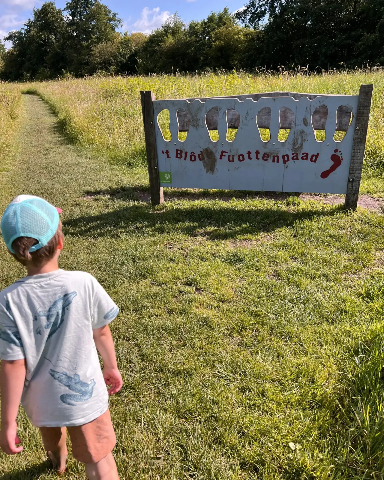 Kind steekt voeten door bord om modder te laten zien op het blotevoetenpad in Opende, Groningen