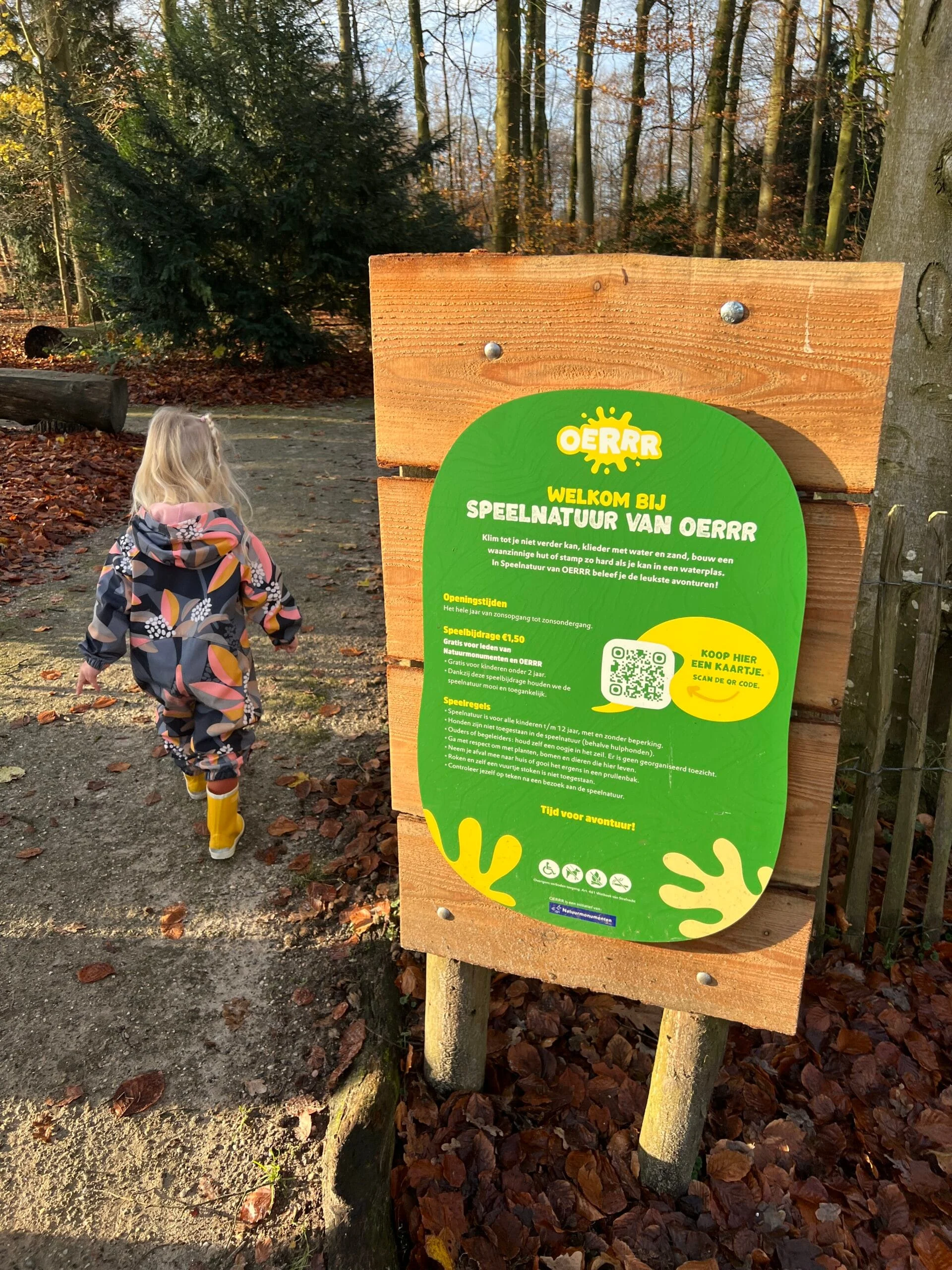 Kind loopt de natuurspeeltuin van OERRR bij Bakkeveen binnen, naast de ingang staat een informatiebord