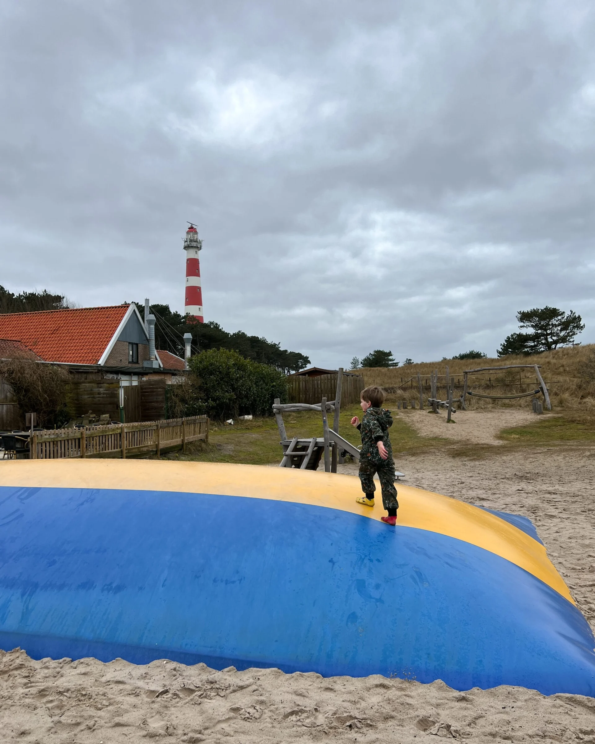 Kind springt op een airtrampoline bij een speeltuin op Ameland met de vuurtoren op de achtergrond