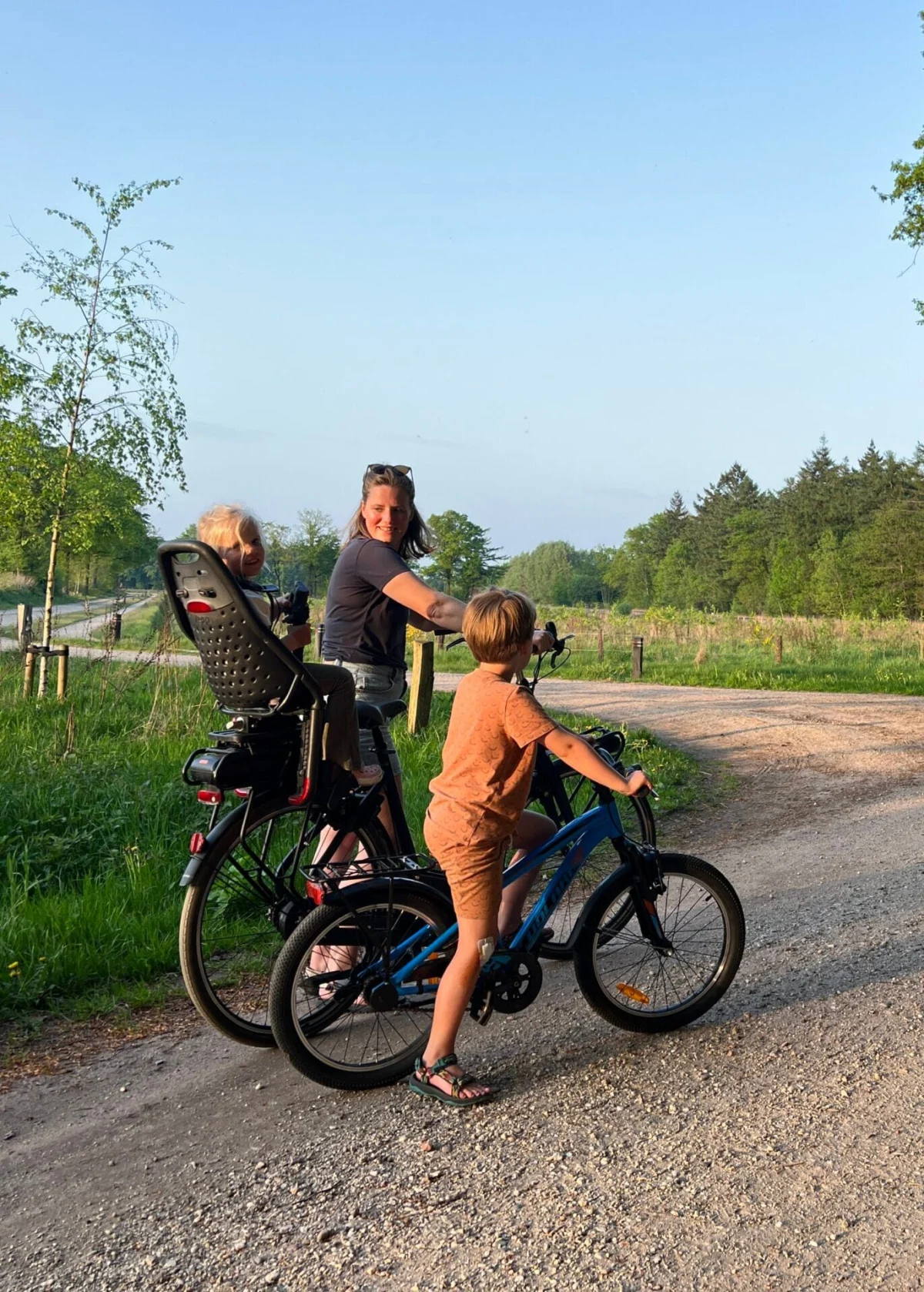Moeder fietst met kind achterop en kind ernaast