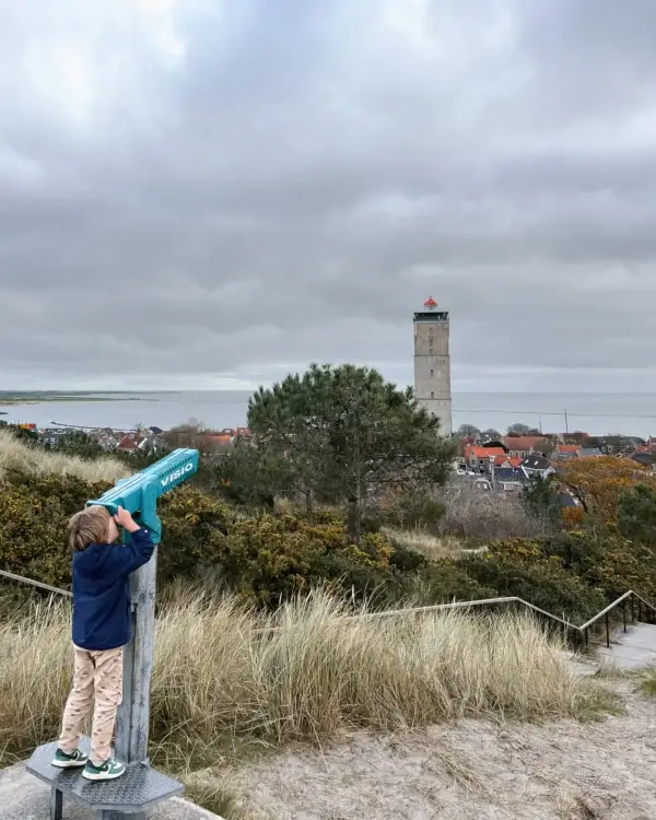 Kind kijkt door een verrekijker naar de Brandaris vanaf een duinuitkijkpunt op Terschelling