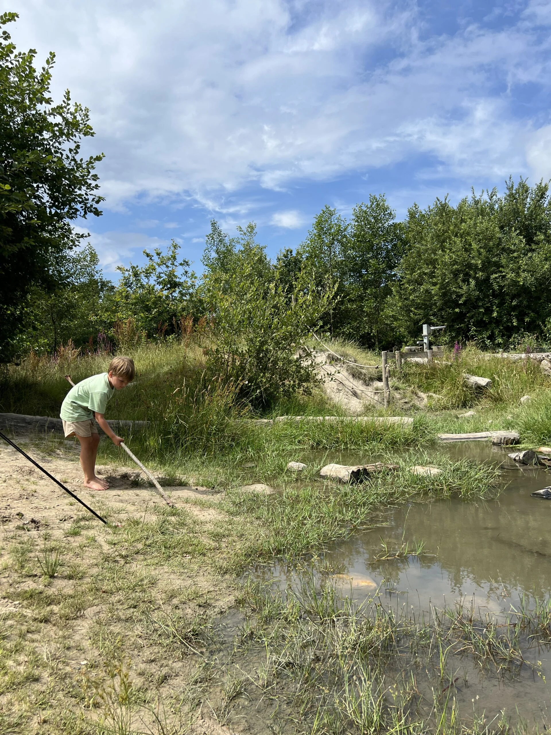 Kind kijkt naar het waterpoeltje in de speelnatuur van OERRR Dwingelderveld in Drenthe een van de leukste natuurspeeltuinen in het Noorden van Nederland