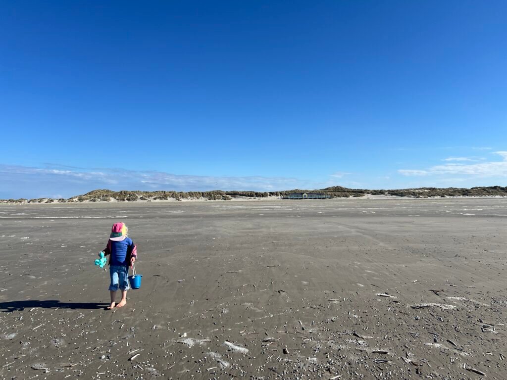 Kind loopt op het brede strand van Terschelling op een zonnige lentedag met blauwe lucht