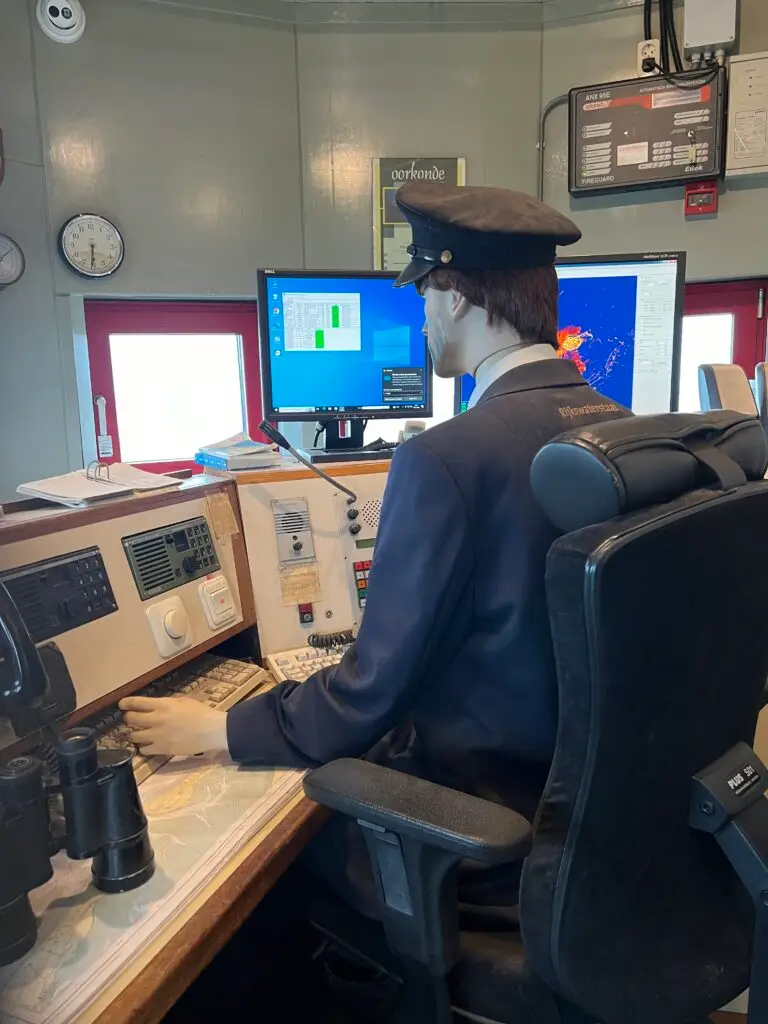 Mannequin van vuurtorenwachter achter uitkijkpaneel in vuurtoren Ameland