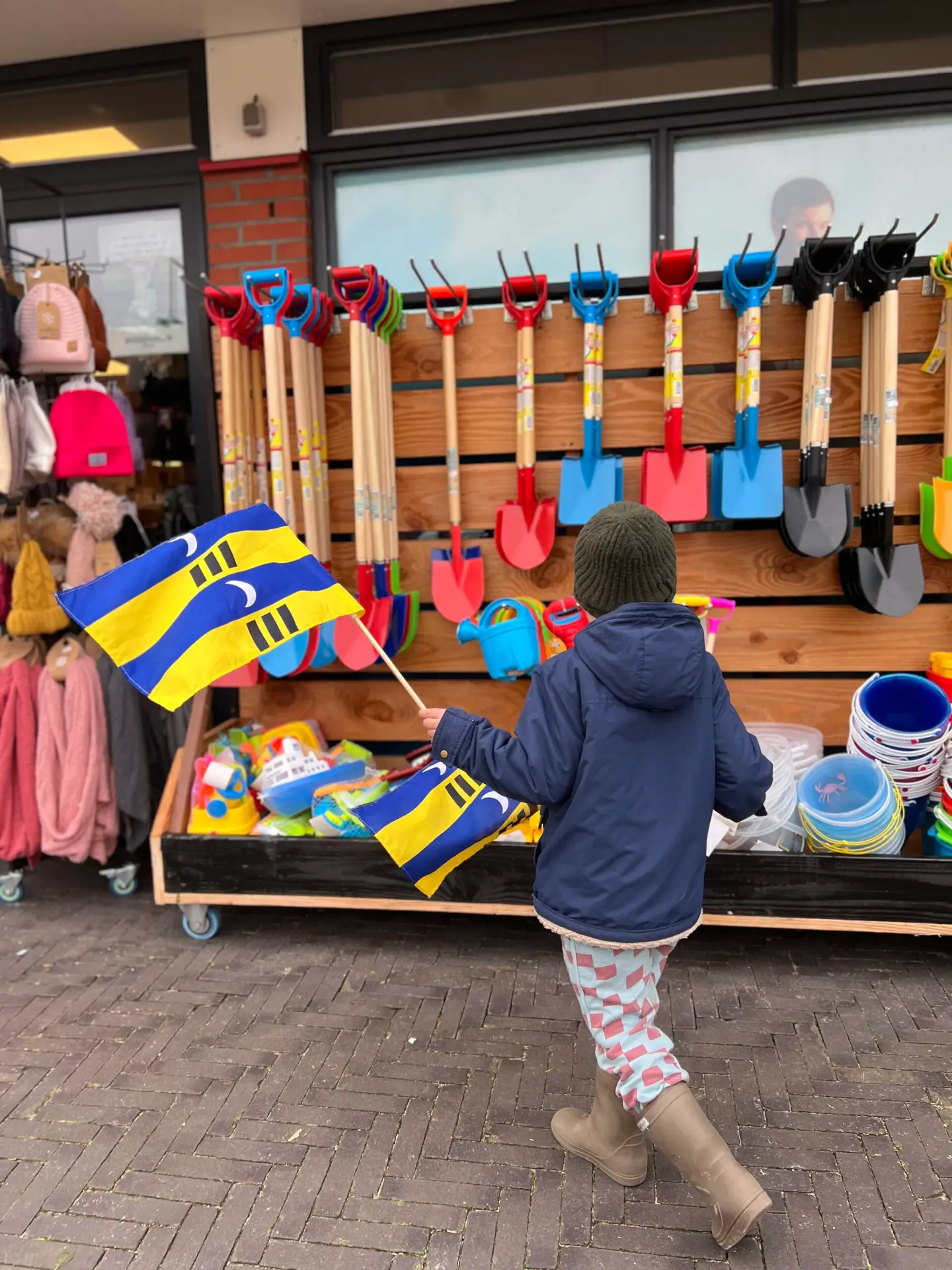 Kind zwaait met de vlag van Ameland bij een winkel, ideaal voor gezinnen die overnachten op Ameland met kinderen