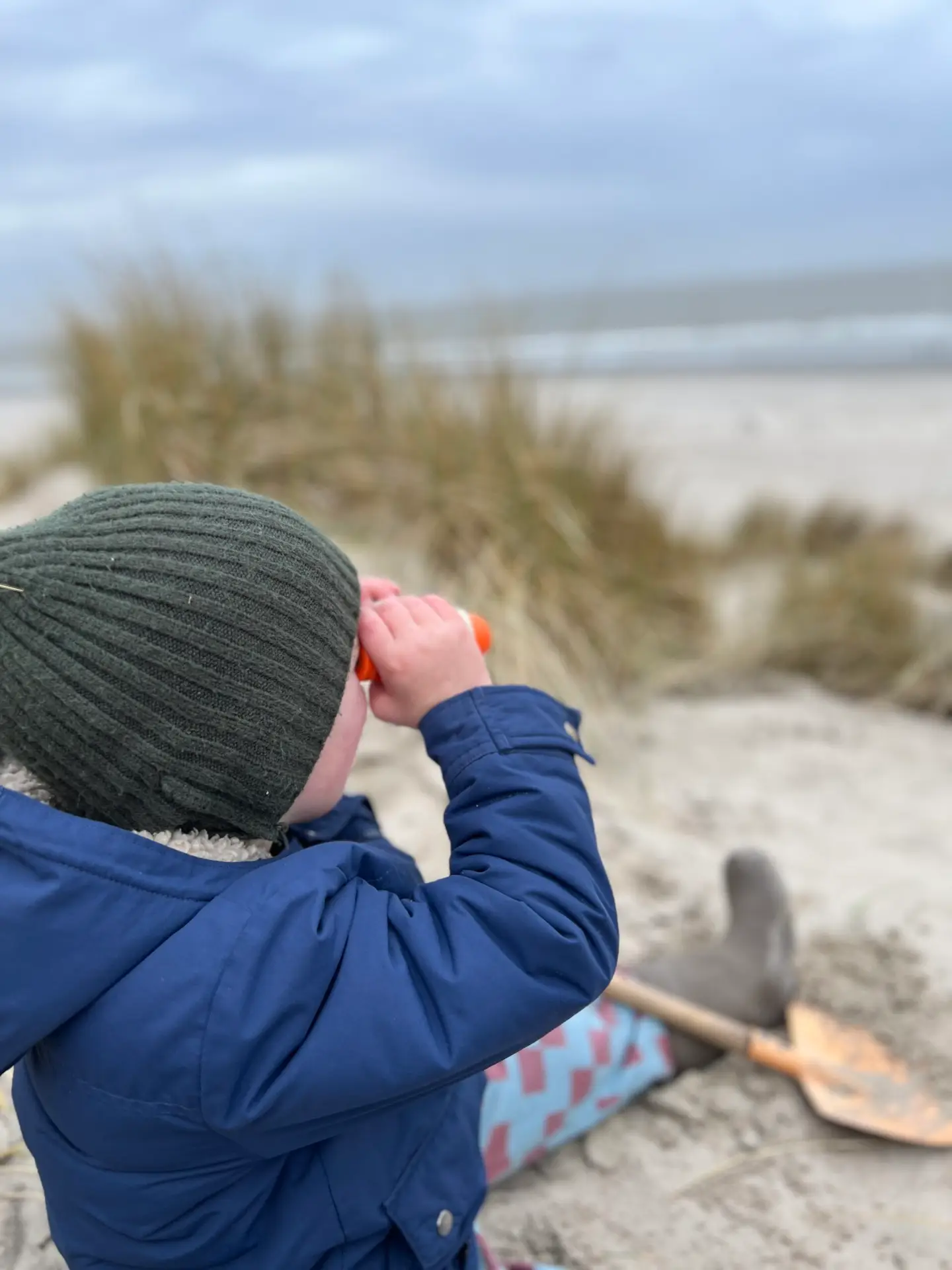 Kind in de duinen van Ameland kijkt met verrekijker naar de zee, ideaal voor gezinnen die overnachten op Ameland met kinderen