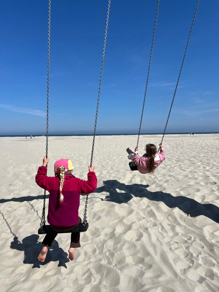 Kinderen schommelen op schommels in het zand op het strand bij Midsland aan Zee op Terschelling