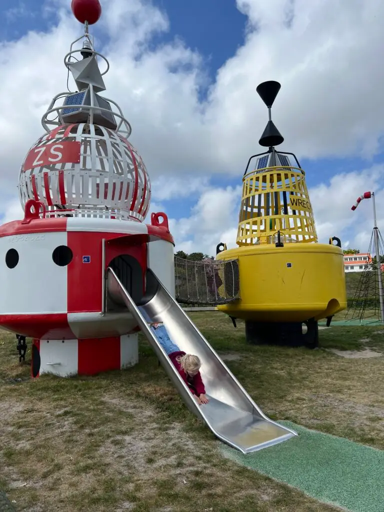 Kind glijdt van de glijbaan in de boeienspeeltuin in de haven van West Terschelling
