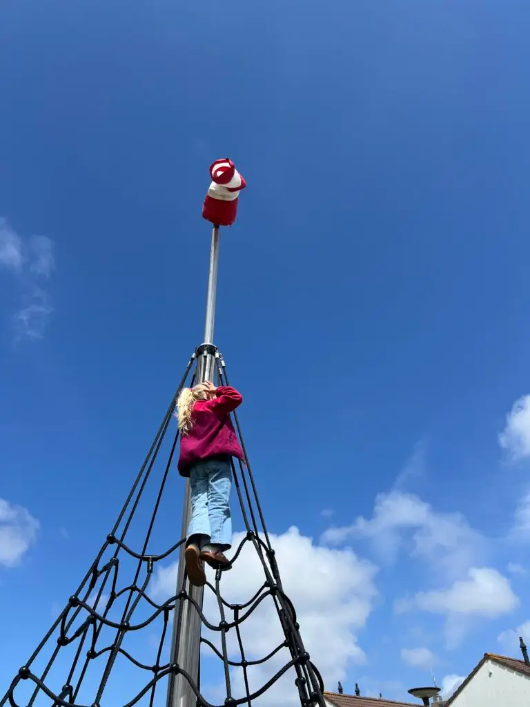 Kind bovenaan de klimtoren in de boeienspeeltuin in de haven van West, met blauwe lucht
