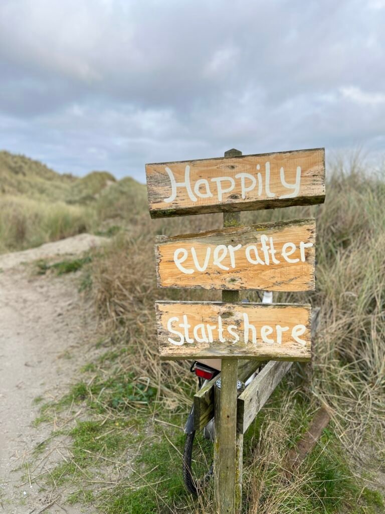 Houten bord met tekst “Happily ever after starts here” bij de strandopgang