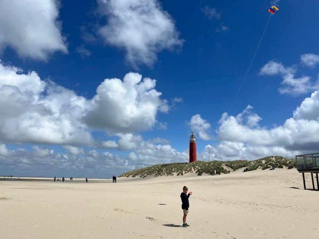 Kind met vlieger op het strand bij het noordelijkste punt van Texel, met de vuurtoren van Texel op de achtergrond