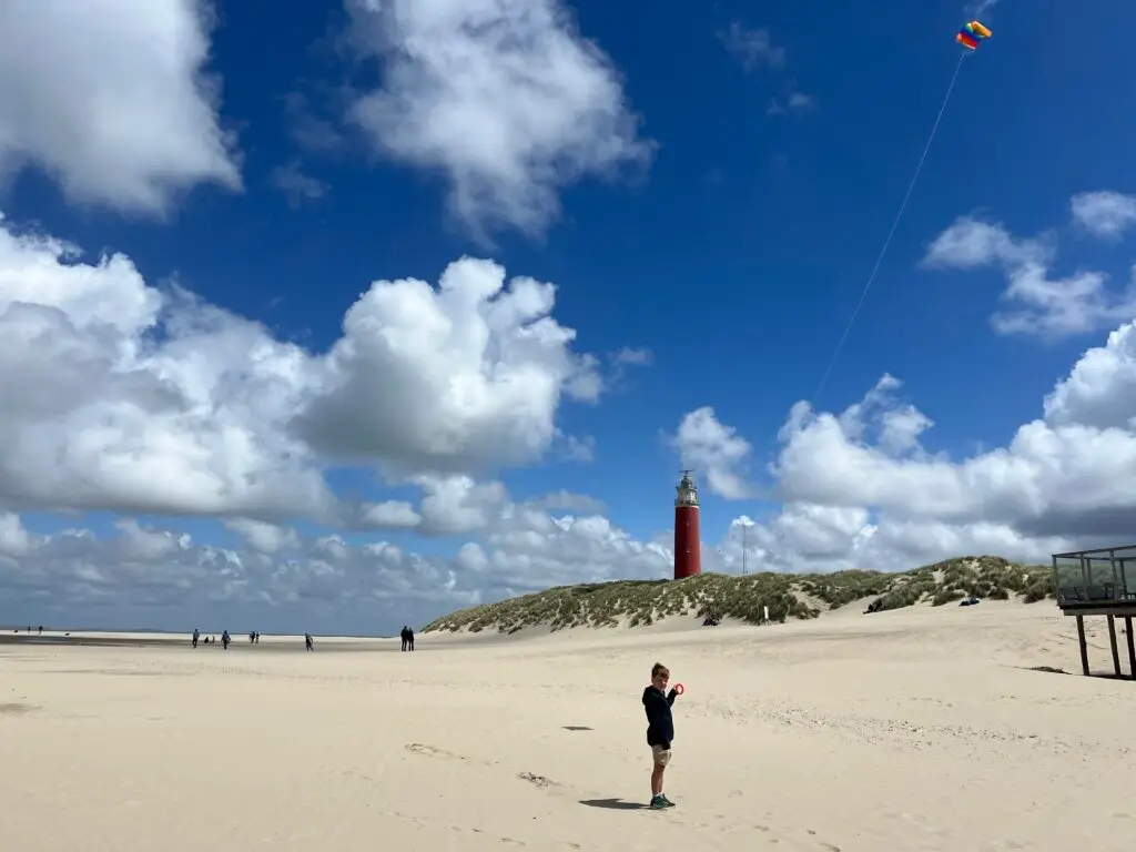 Kind met vlieger op het strand bij het noordelijkste punt van Texel, met de vuurtoren van Texel op de achtergrond