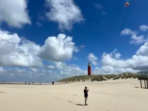 Kind met vlieger op het strand bij het noordelijkste punt van Texel, met de vuurtoren van Texel op de achtergrond