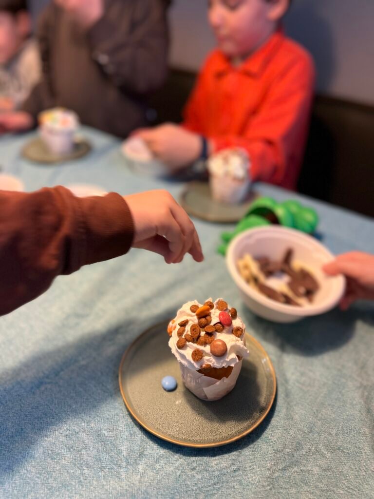 Kind versiert een cakeje met slagroom en gekleurde spikkels tijdens een kinderfeestje
