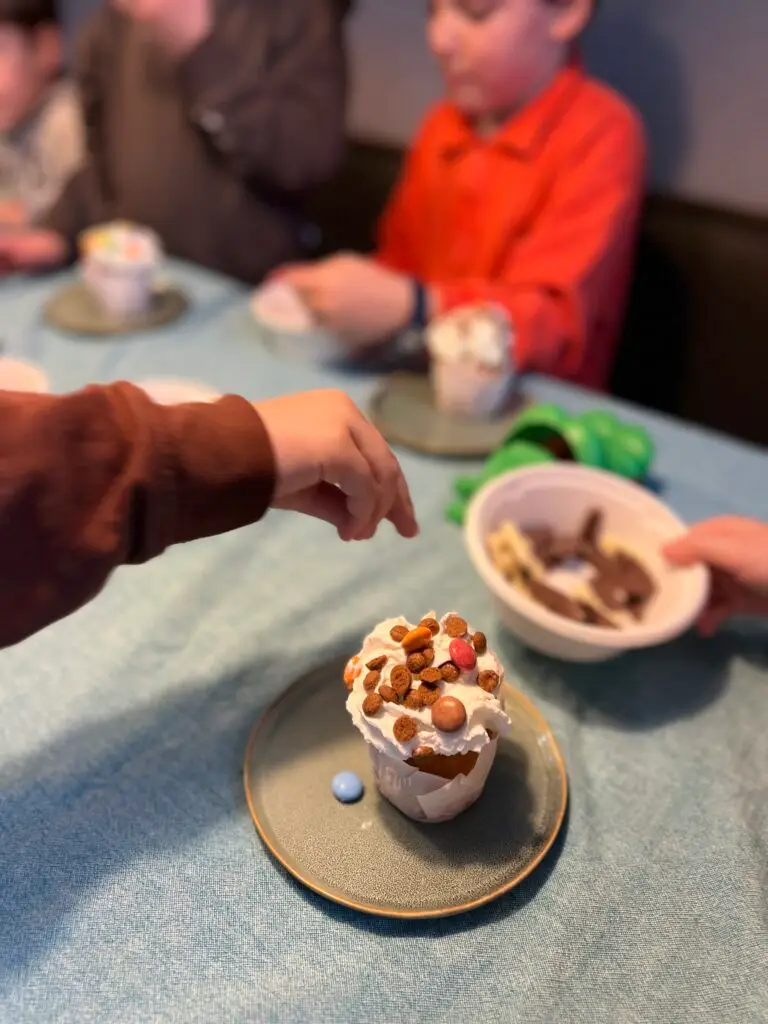 Kind versiert een cakeje met slagroom en gekleurde spikkels tijdens een kinderfeestje