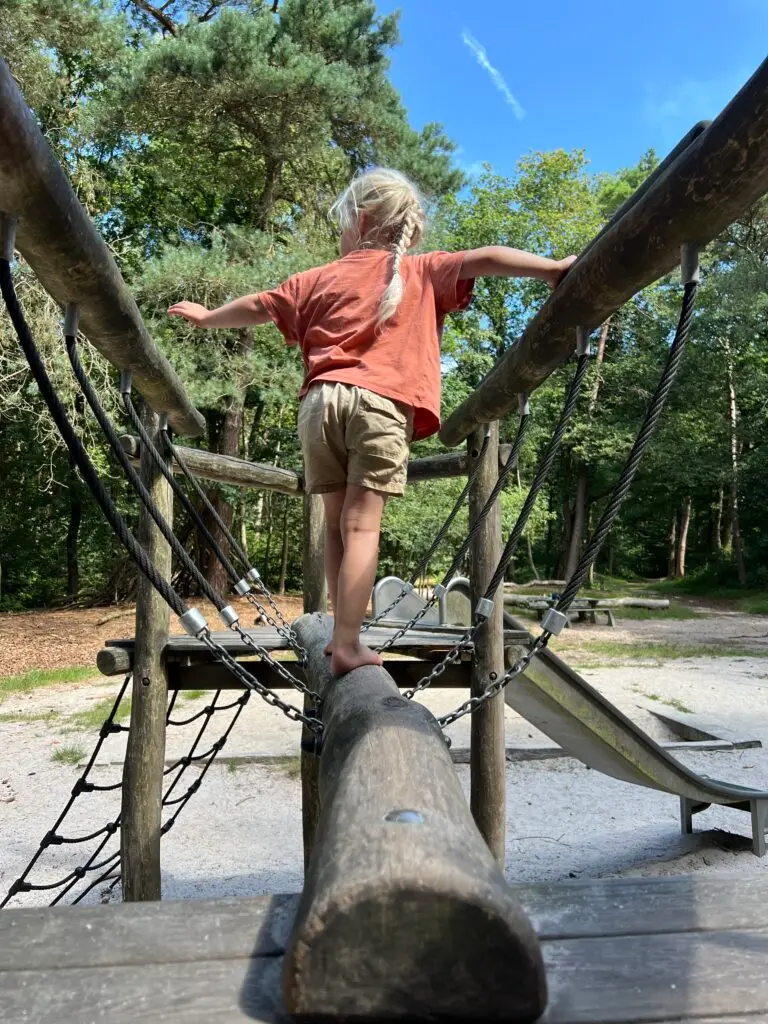 Kind balanceert op een houten balk op een speeltoestel in het Blauwe Bos