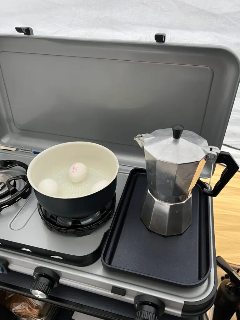 Camping gasstel met kokende eieren en percolator ernaast
