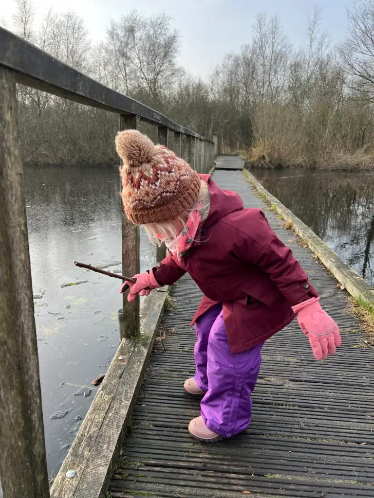 Kind tikt met een tak op het ijs bij natuurgebied De Deelen in Friesland
