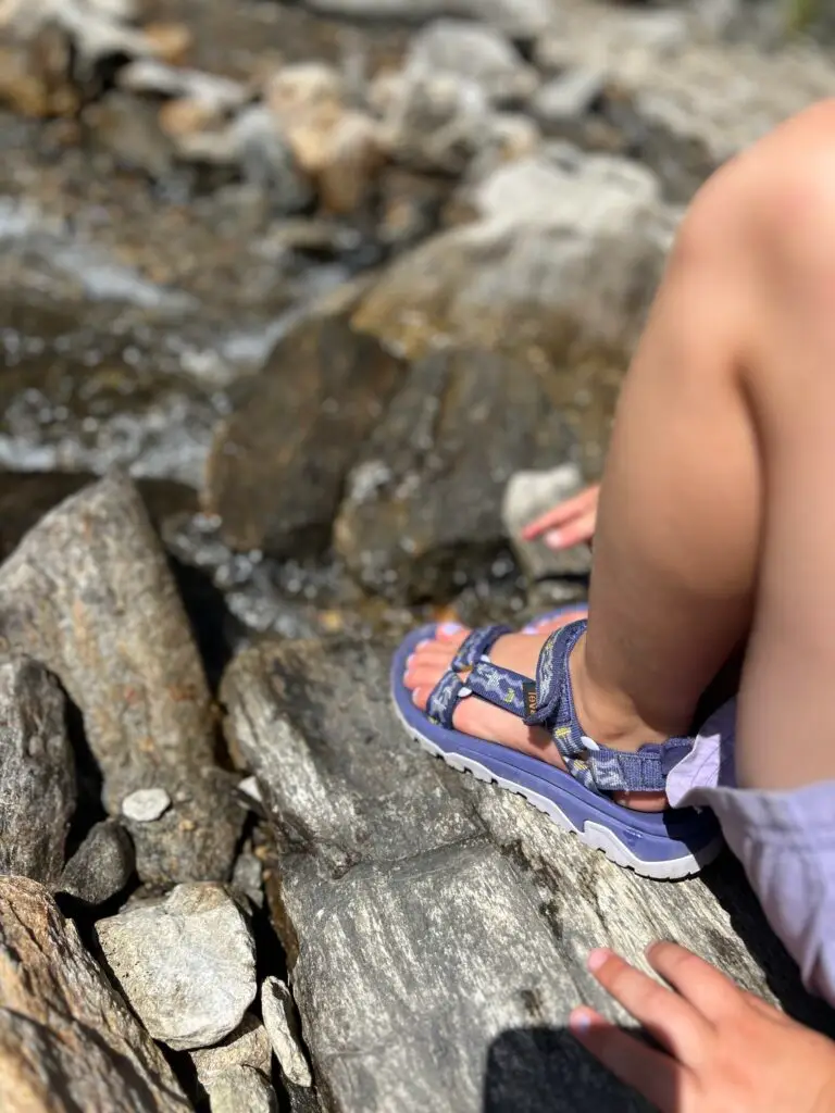 Kind met Teva sandalen staat in een beekje bij een vakantie in de bergen met kinderen