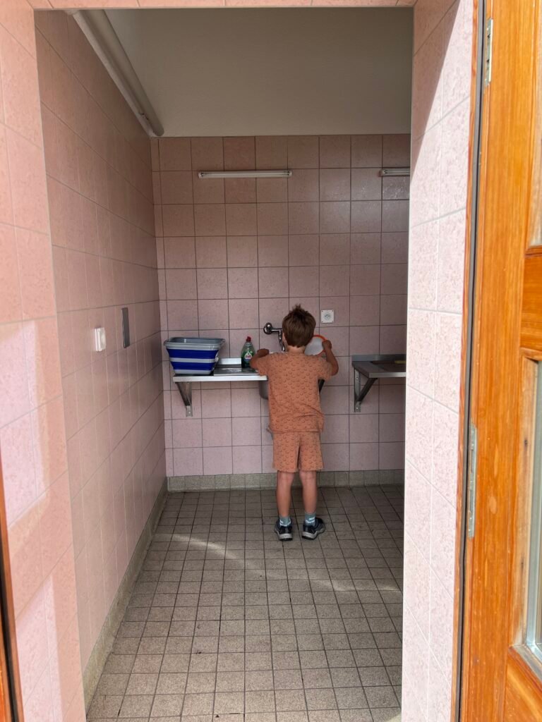 Kind doet de afwas met opvouwbare afwasteil op de camping, handige kampeerspullen