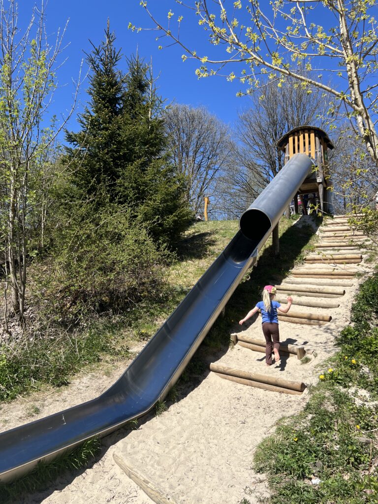 Kind klimt trap op naar lange glijbaan van de Robinsonspielplatz in de Harz in de lente